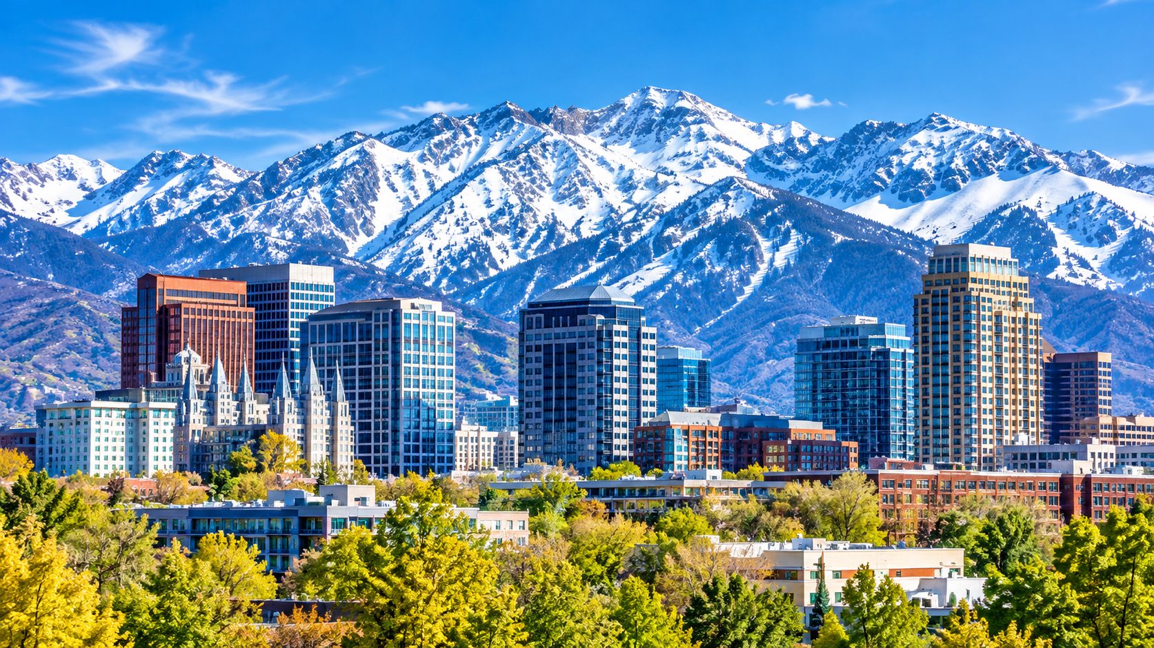 Snow-capped Wasatch mountains rising behind a Utah city skyline